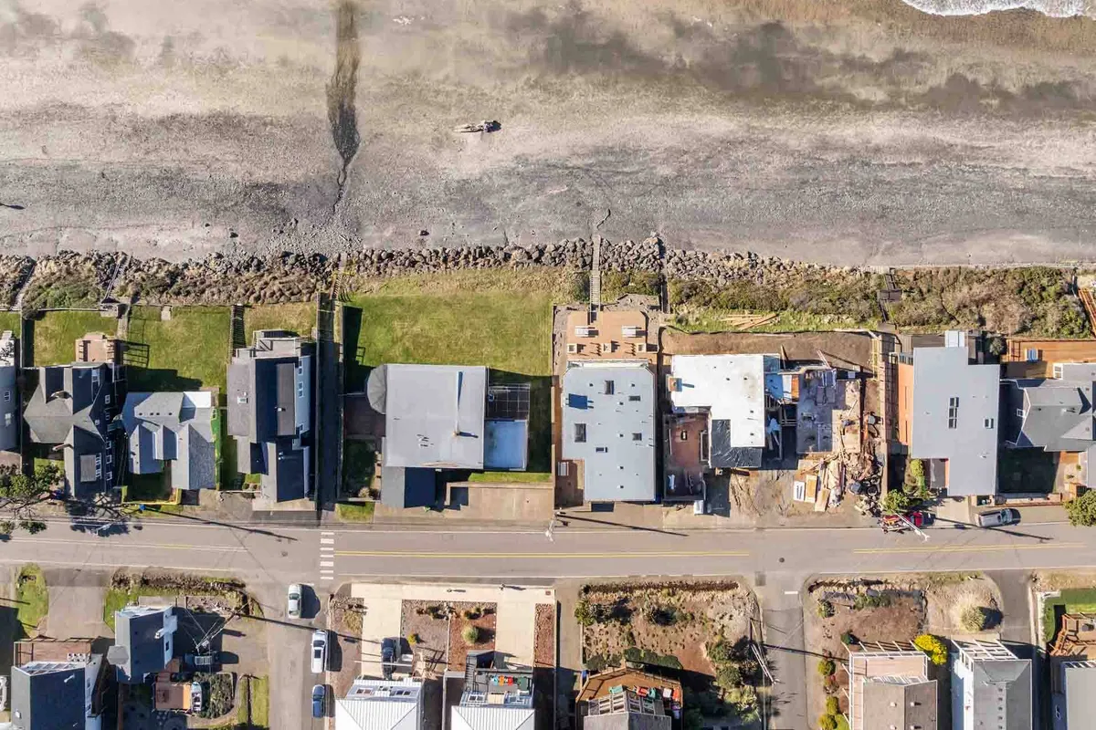 A panoramic view of beachfront homes lining a coastal road, with waves gently hitting the shore. The scene evokes the tranquility and accessibility of the beach, highlighting options for beach walks and group activities along the shoreline.