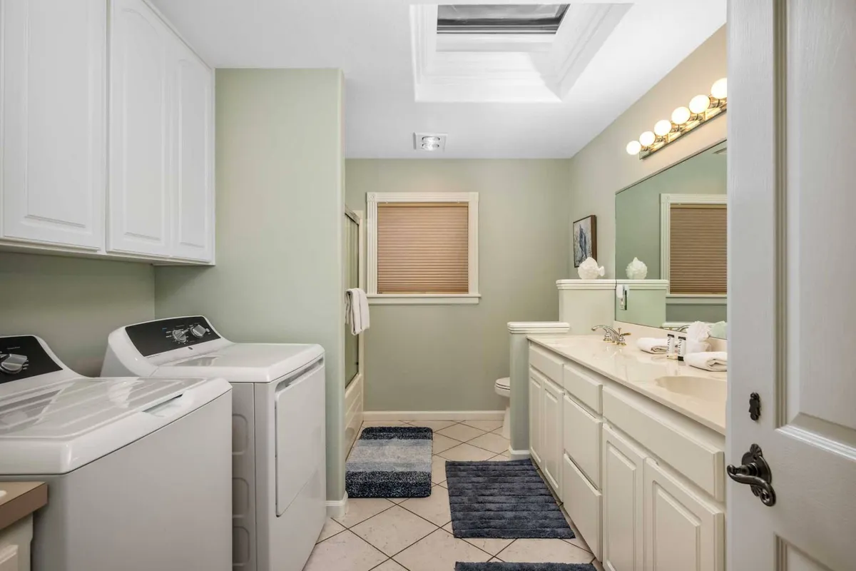 A bright, functional laundry area with a washer and dryer, stylish vanity with mirror, and a skylight flooding the space with natural light. The design is tidy and inviting, perfect for both short and extended stays.