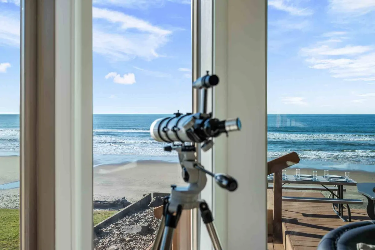 A deck area featuring a telescope focused on the sweeping ocean view, suggesting moments of stargazing or watching marine life. The atmosphere is calm, emphasizing connection to the natural coastal beauty.