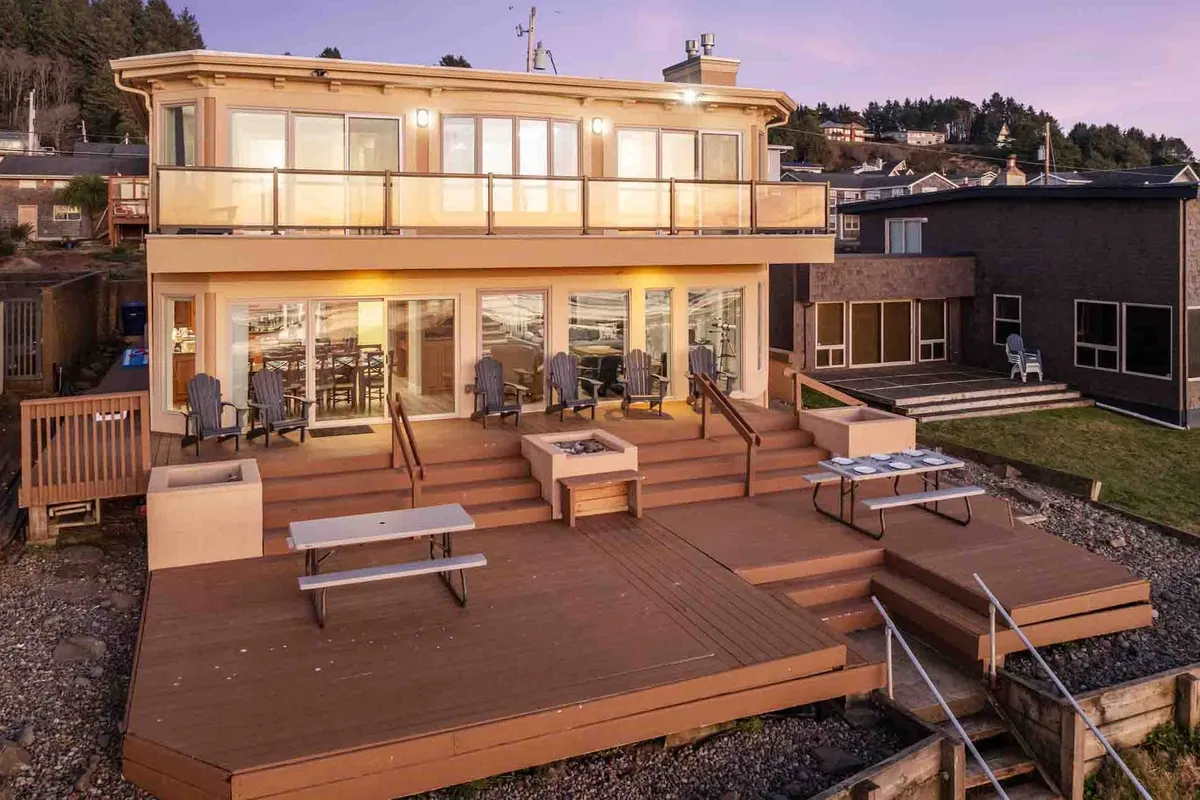 This image captures a spacious deck area with large glass doors leading into the house, featuring an inviting fire pit and multiple seating options perfect for gatherings. The outdoor space is arranged for socializing, dining, and enjoying the sunset, reflecting opportunities for relaxation and group entertainment after a day of activities.