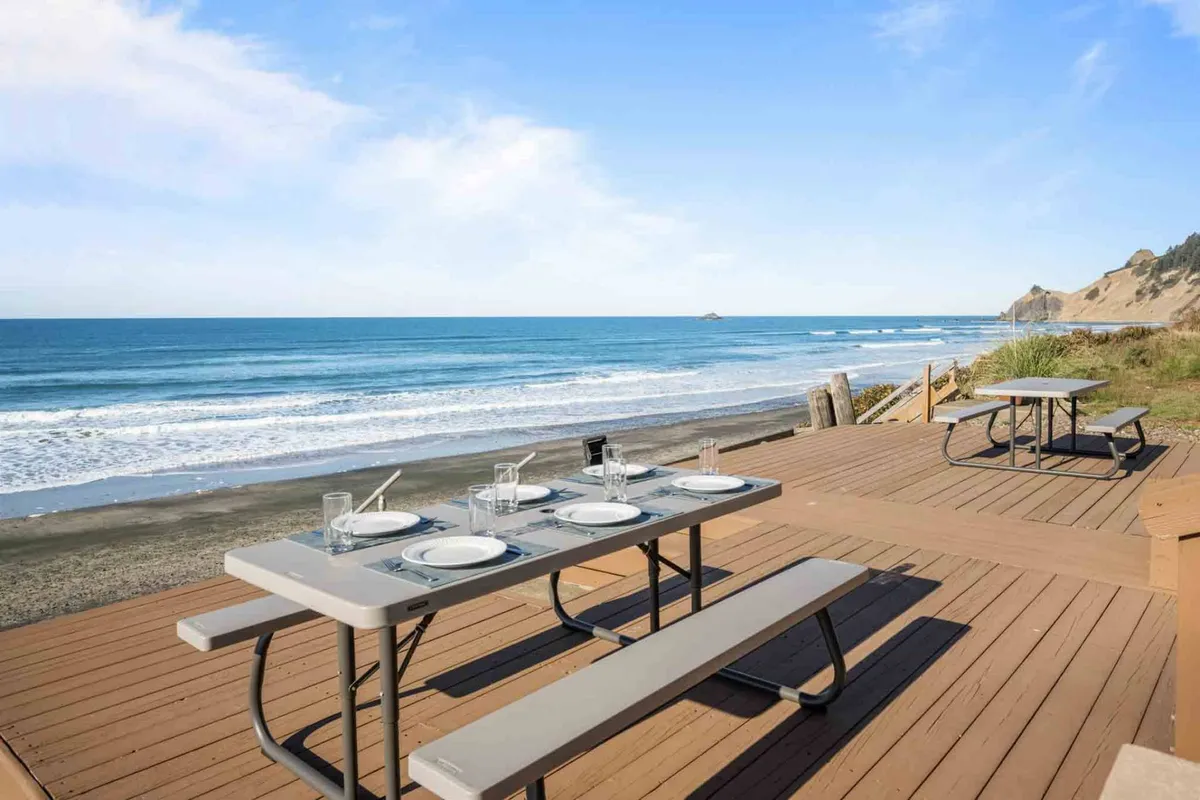 A serene exterior deck with an ocean view, dining setup, and beachside seating arrangement. The scene suggests relaxed outdoor living—ideal for unwinding, dining, or simply taking in the coastal breeze.