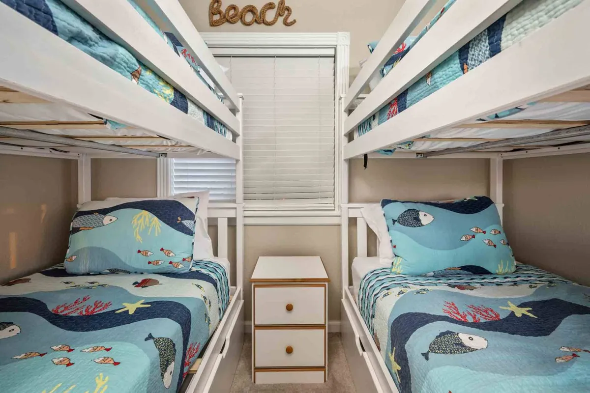 A playful and inviting bunk bedroom with colorful bedding on built-in bunk beds, accented by a cheerful decorative sign. The room exudes warmth and is ideal for children or groups, hinting at bedtime stories and giggles.