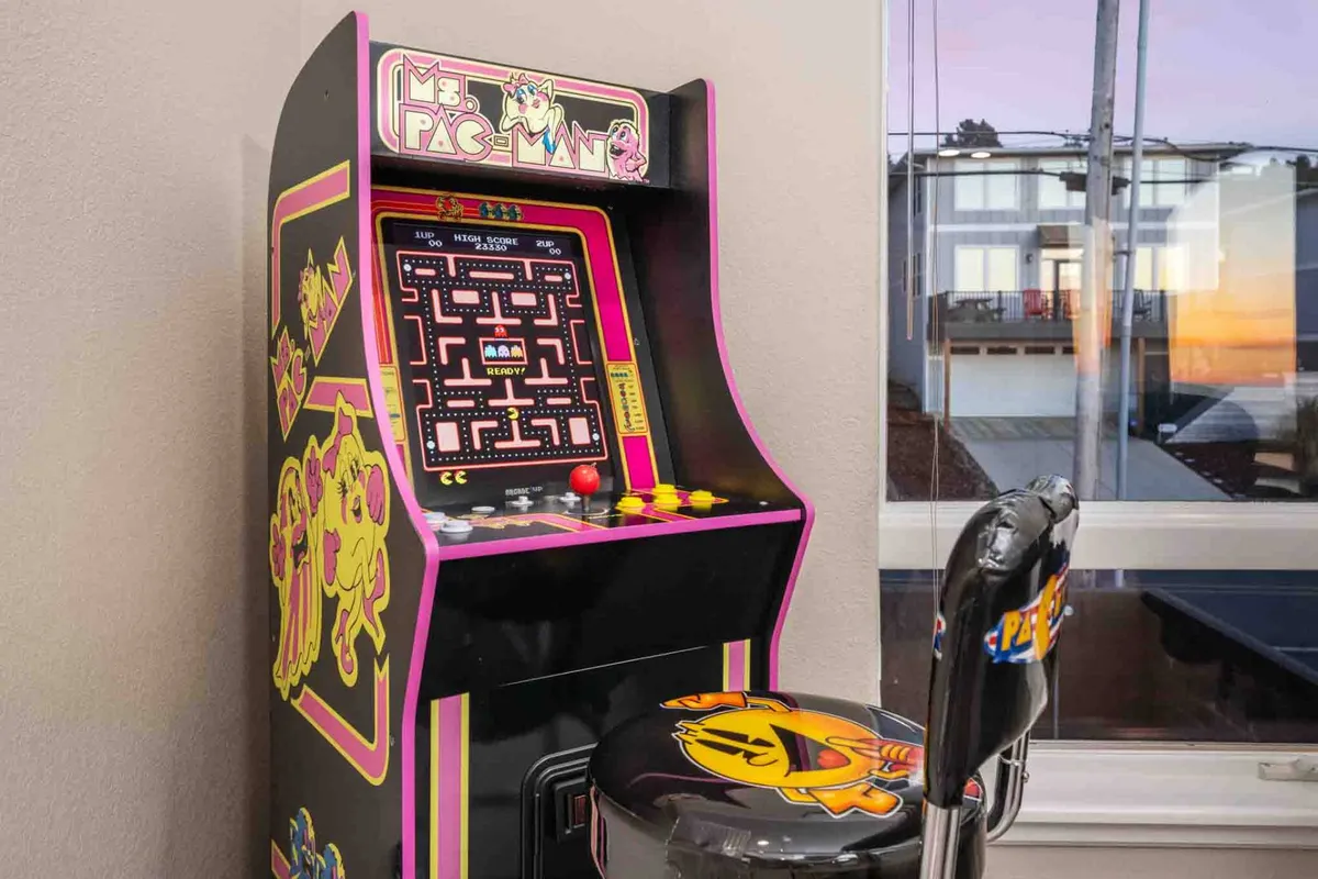 The scene highlights a Ms. Pac-Man arcade machine with a matching themed stool, evoking nostalgia and fun. The game setup is clearly designed for competitive play and encourages interactive entertainment, reflecting the playful spirit described in the section.