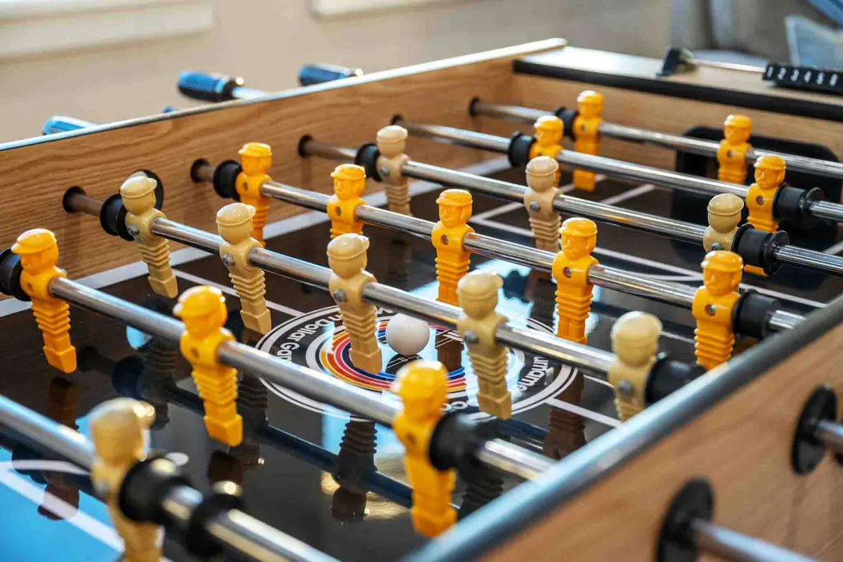 A foosball table with colorful player figurines is the centerpiece in a casual game room setting. The energetic vibe is perfect for small tournaments, friendly matches, and group fun, appealing to both kids and adults.