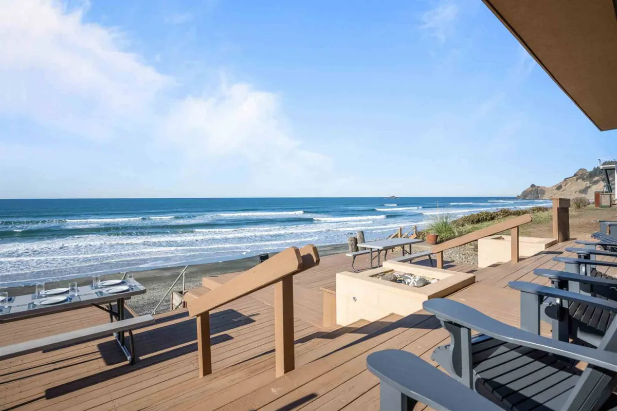 An expansive deck with comfortable seating and a fire pit overlooks the rolling ocean waves. The deck invites guests to relax, socialize, or take in the sunset, seamlessly connecting the indoor workspace with the natural beauty of the coastline.
