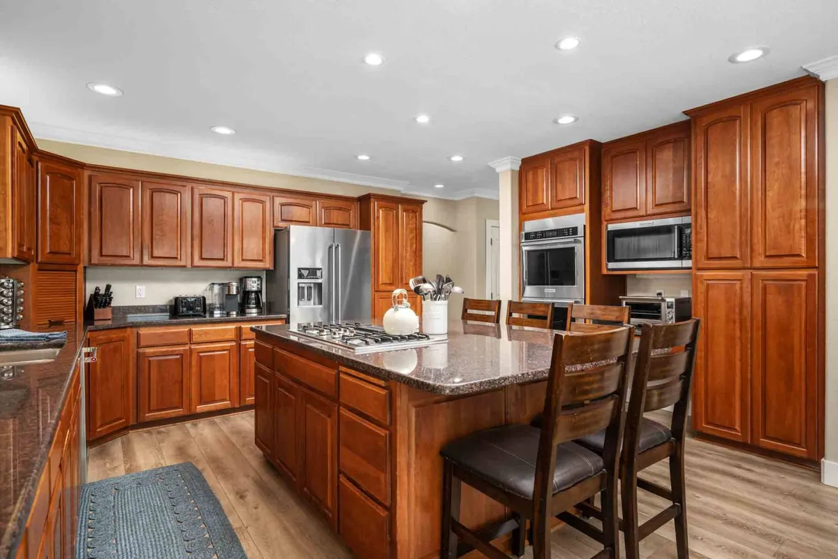 A modern chef’s kitchen with sleek granite countertops, stainless steel appliances, and wooden cabinetry. The large kitchen island offers ample space for meal prep, casual breakfasts, or happy hour gatherings, inviting everyone to be part of the culinary action.