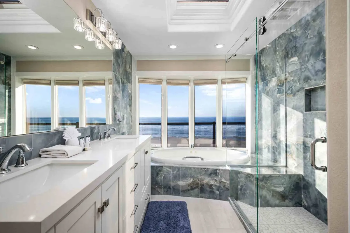 A spa-inspired bathroom featuring a modern standalone bathtub positioned by large windows overlooking the ocean, complemented by a sleek vanity. The scene is bathed in natural light, creating an atmosphere of relaxation and luxury.