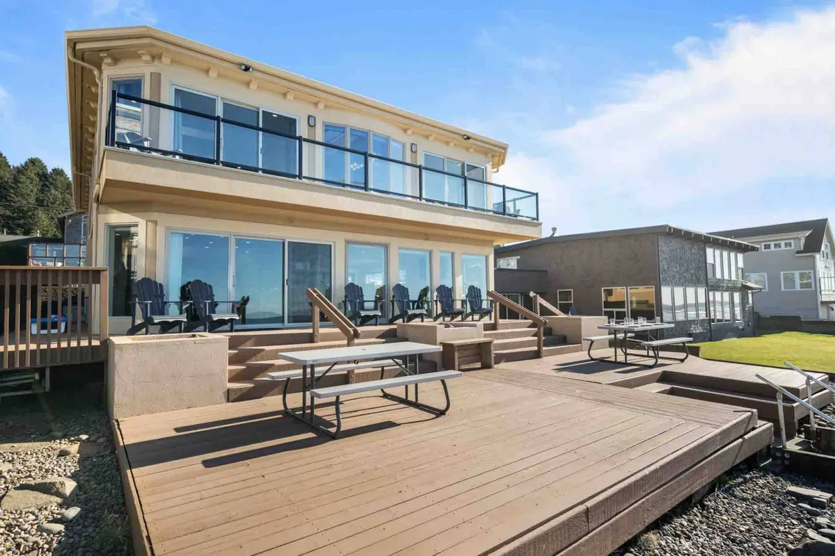 A cheerful exterior with large glass windows, deck seating, and an expansive view of the ocean. The outdoor seating area is ideal for gatherings, quiet reflection, or enjoying the natural surroundings.