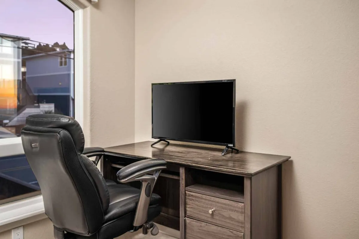 A dedicated workspace featuring a desk, ergonomic chair, and computer monitor, set beside a window that offers a calming view outside. The space feels bright and focused—ideal for productive work sessions.