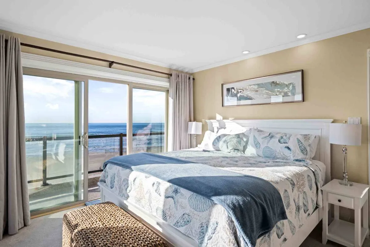 A light-filled bedroom with a comfortable bed dressed in soft, high-end bedding, large windows framing a spectacular ocean view, and tranquil décor. The setup exudes peace and offers a rejuvenating ambiance.